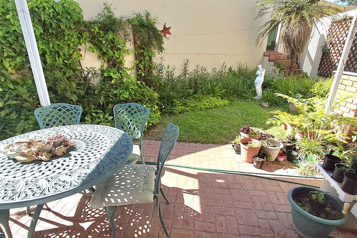 A private rear courtyard featuring brick paving, established garden beds, and a staircase leading to an upper level.