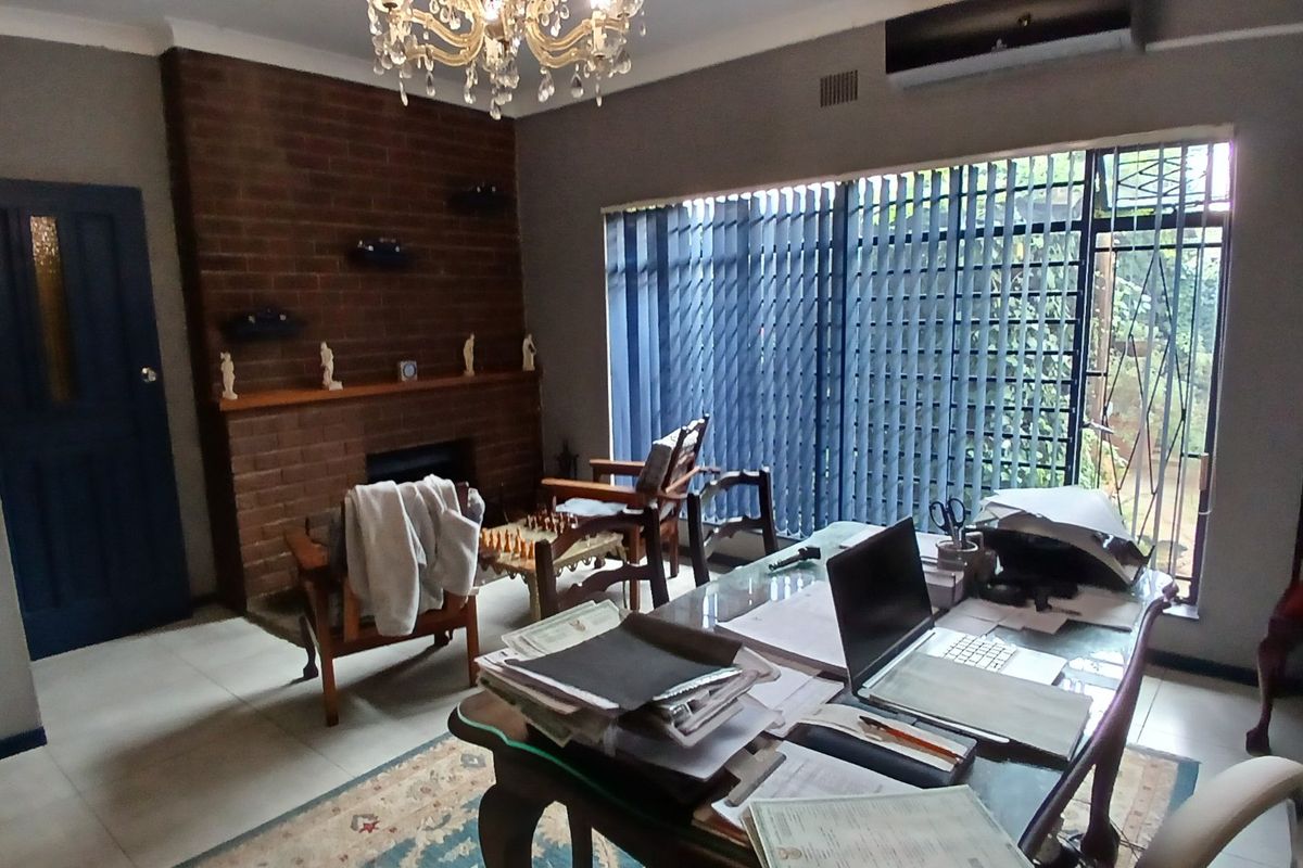 A living room featuring a brick fireplace, tiled flooring, and a split-system air conditioner, with large windows covered by vertical blinds.