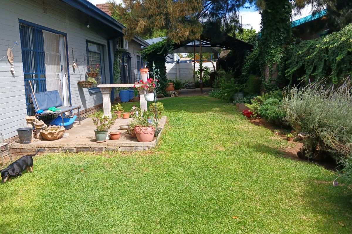 A private rear garden featuring a paved patio area, established lawn, and mature garden beds adjacent to the house.