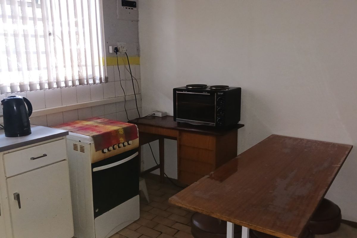 A functional kitchen area featuring basic cabinetry, a tiled splashback, and vertical blinds, currently showing signs of wear and dated finishes.