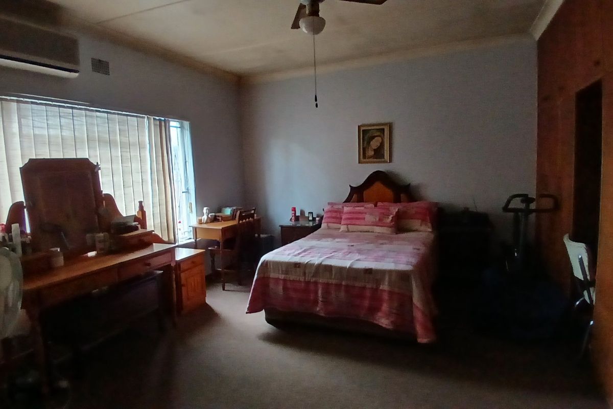 Spacious bedroom featuring built-in cupboards, a ceiling fan, and an air conditioning unit, offering a functional layout with natural light.
