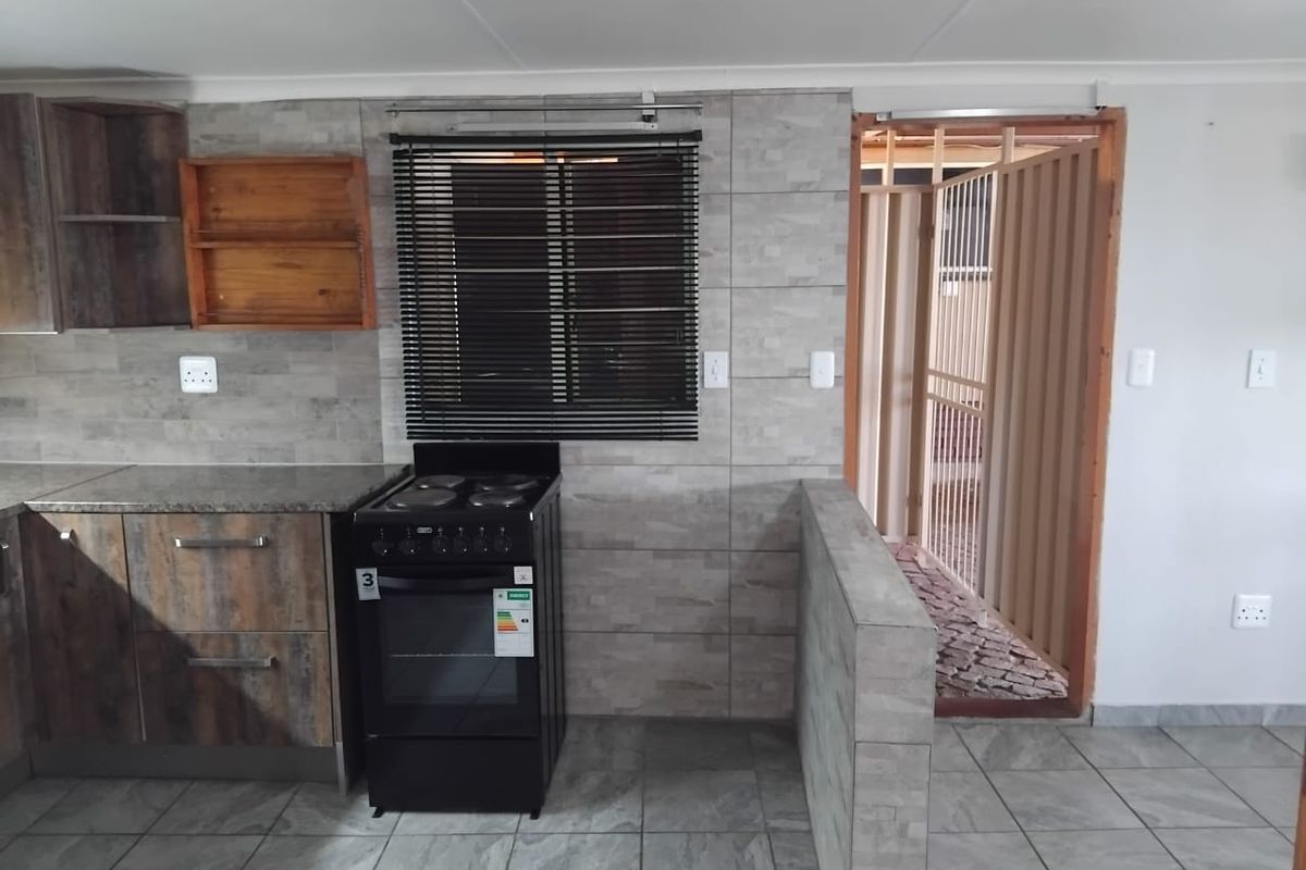 A functional kitchen featuring stone-look tiled walls, built-in cabinetry, and a freestanding stove, with direct access to an outdoor area.