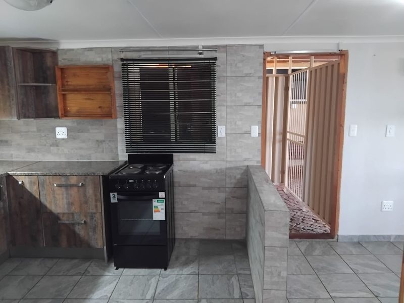 A functional kitchen featuring stone-look tiled walls, built-in cabinetry, and a freestanding stove, with direct access to an outdoor area.