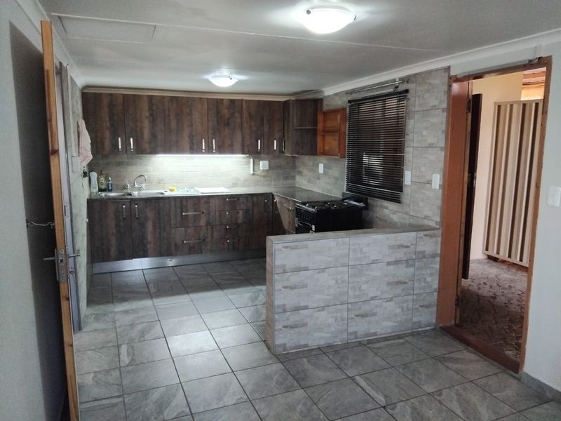 A functional kitchen featuring dark wood-look cabinetry, tiled splashbacks, tiled flooring, and a freestanding stove, offering a clean and practical workspace.