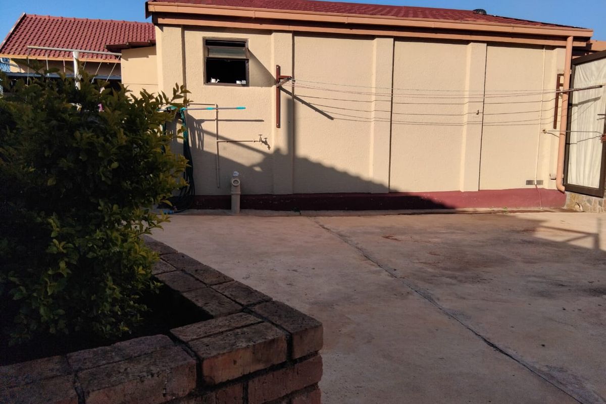 Rear exterior area featuring concrete paving, a brick planter, and functional utility fixtures including a water tap and washing line.