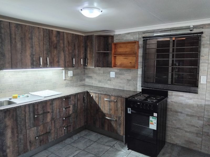 A well-maintained kitchen featuring dark wood-look cabinetry, stone-effect countertops, tiled backsplash, and a modern freestanding electric stove with integrated under-cabinet lighting.