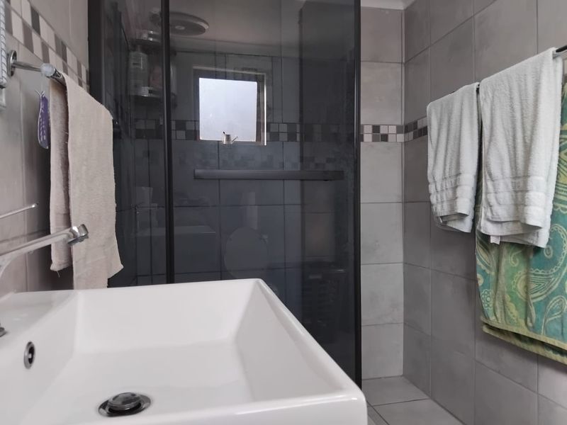 A functional bathroom featuring a modern basin, tiled walls, and a glass-enclosed shower area with a small window for ventilation.