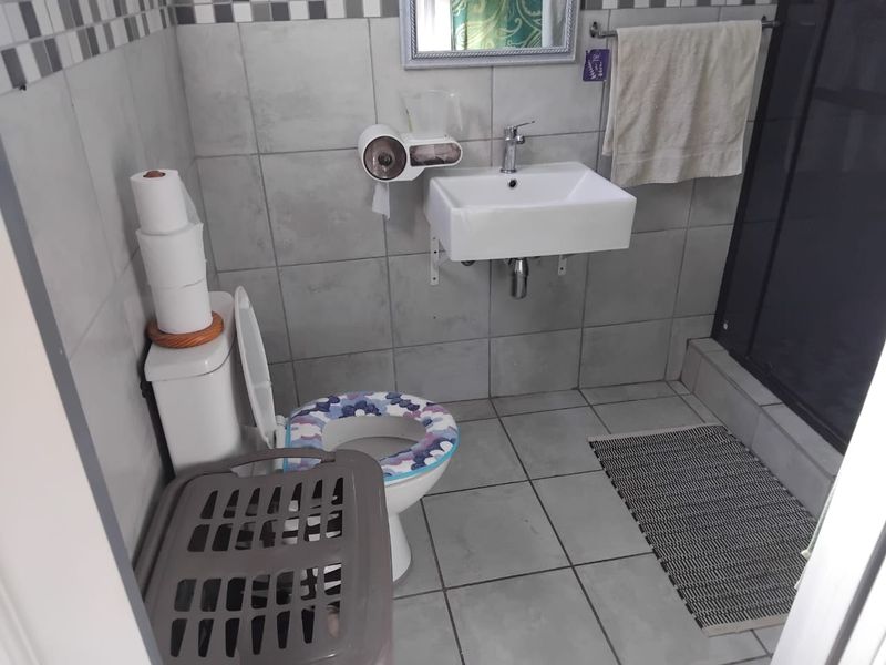 A functional bathroom featuring a wall-mounted basin, toilet, and shower enclosure with neutral grey wall and floor tiling.
