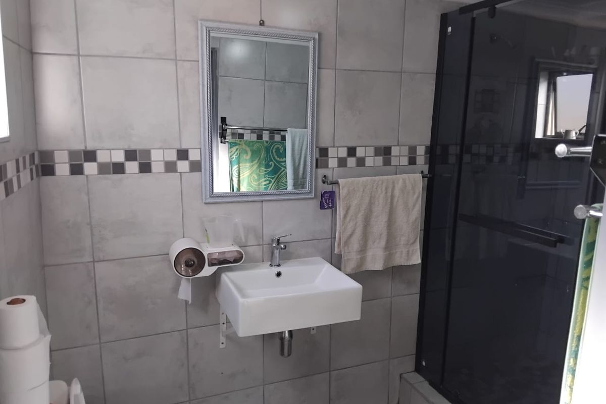 A functional bathroom featuring a wall-mounted basin, tiled walls with a decorative border, and a glass-enclosed shower.