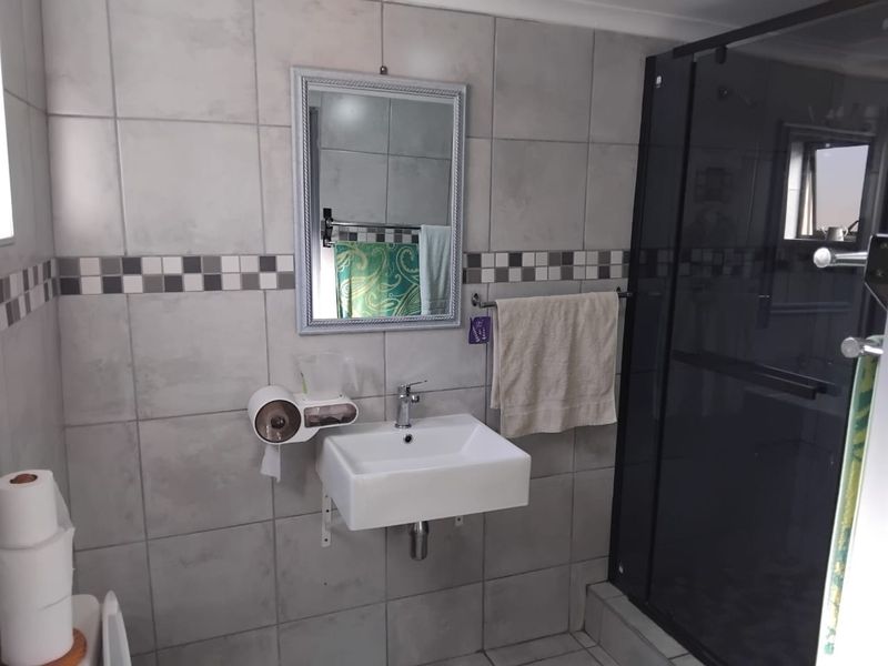 A functional bathroom featuring a wall-mounted basin, tiled walls with a decorative border, and a glass-enclosed shower.