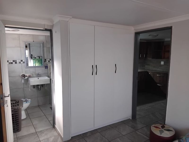 Bedroom featuring built-in cupboards, tiled flooring, and direct access to an en-suite bathroom and adjacent kitchen area.
