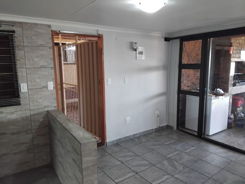 An open-plan living area featuring tiled flooring, a stone-cladding accent wall, and a sliding glass door leading to an outdoor space.