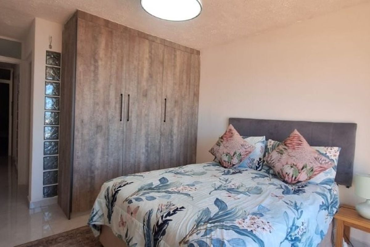 A well-maintained bedroom featuring a large wood-finish built-in wardrobe, a unique glass block accent wall, and neutral tiled flooring.