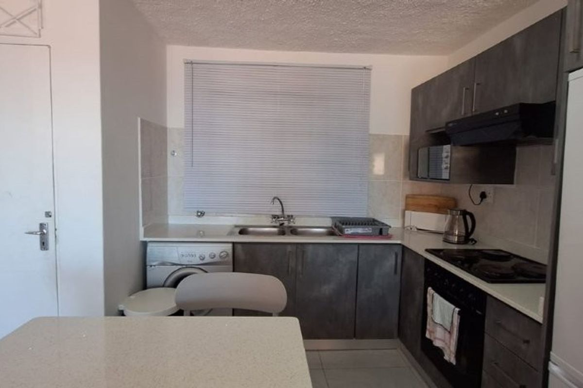 A functional kitchen featuring dark grey cabinetry, a double sink, built-in oven with hob, and a tiled backsplash.