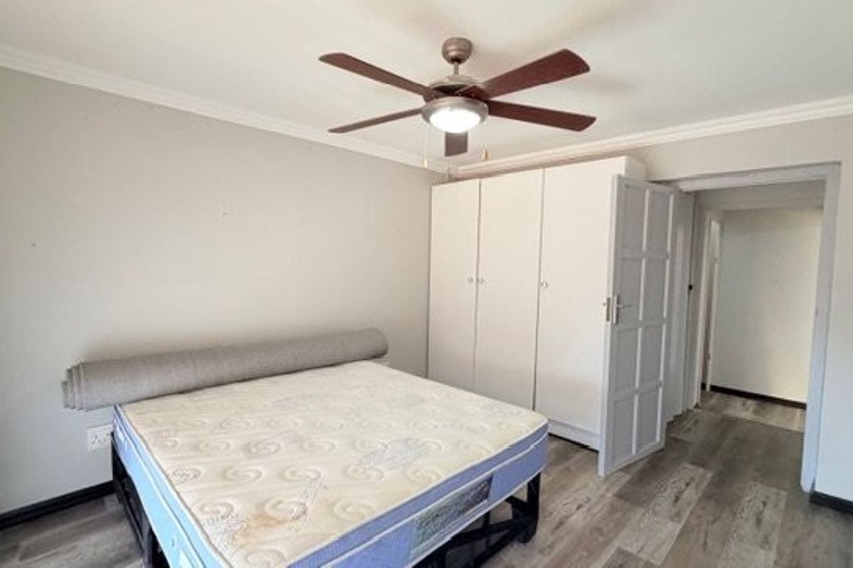 A bedroom featuring laminate flooring, a ceiling fan, and built-in cupboards, offering a functional and neutral living space.