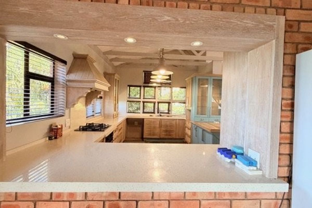 A charming kitchen featuring exposed brick walls, stone countertops, timber cabinetry, and exposed ceiling beams, creating a warm and rustic aesthetic.