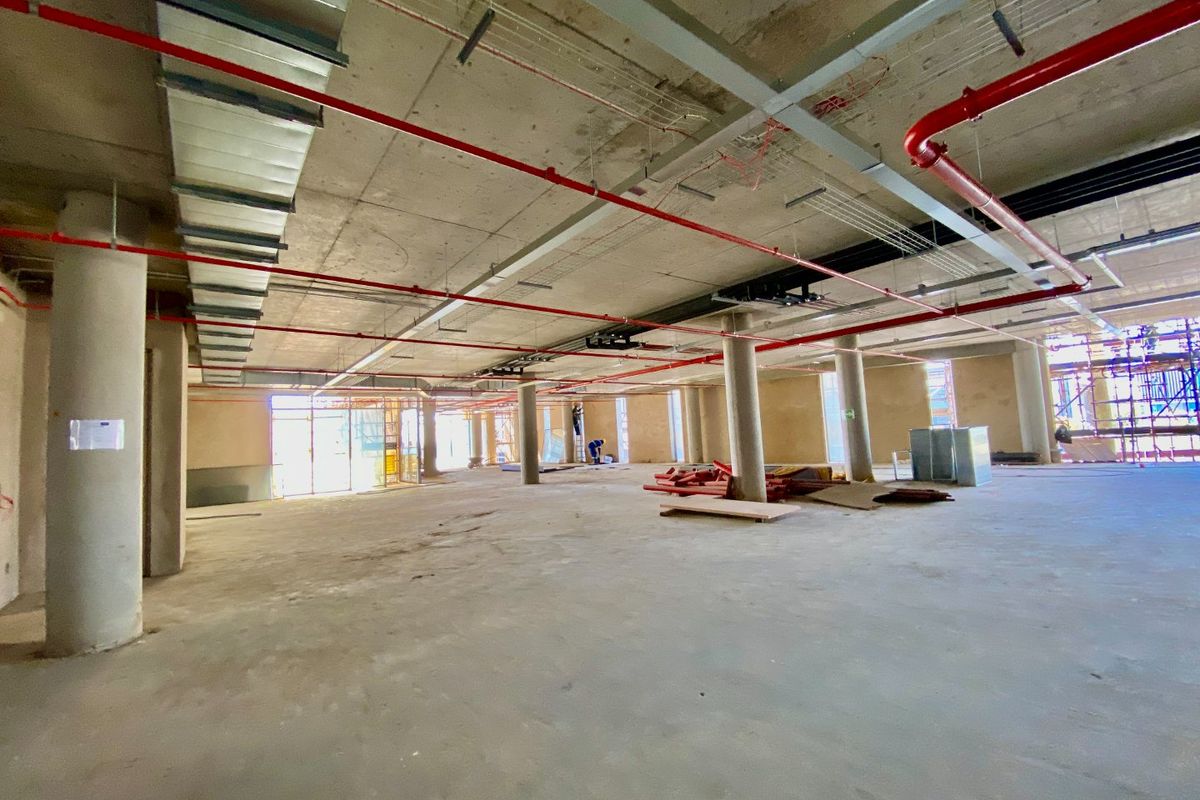 Large open-plan commercial space currently under construction, featuring exposed concrete ceilings, structural columns, and industrial fire sprinkler and HVAC systems.