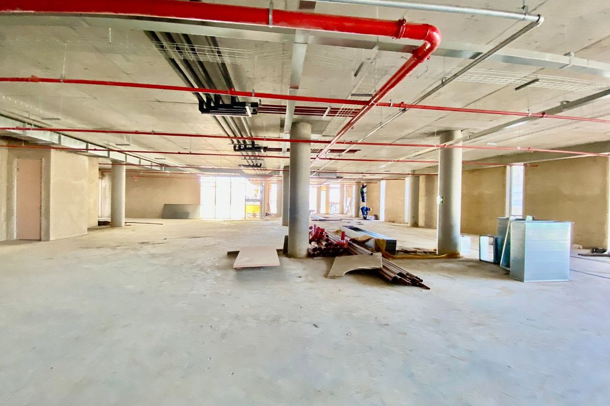 A large, open-plan commercial space in shell condition, featuring exposed concrete ceilings, support columns, and fire sprinkler infrastructure, ready for custom fit-out.