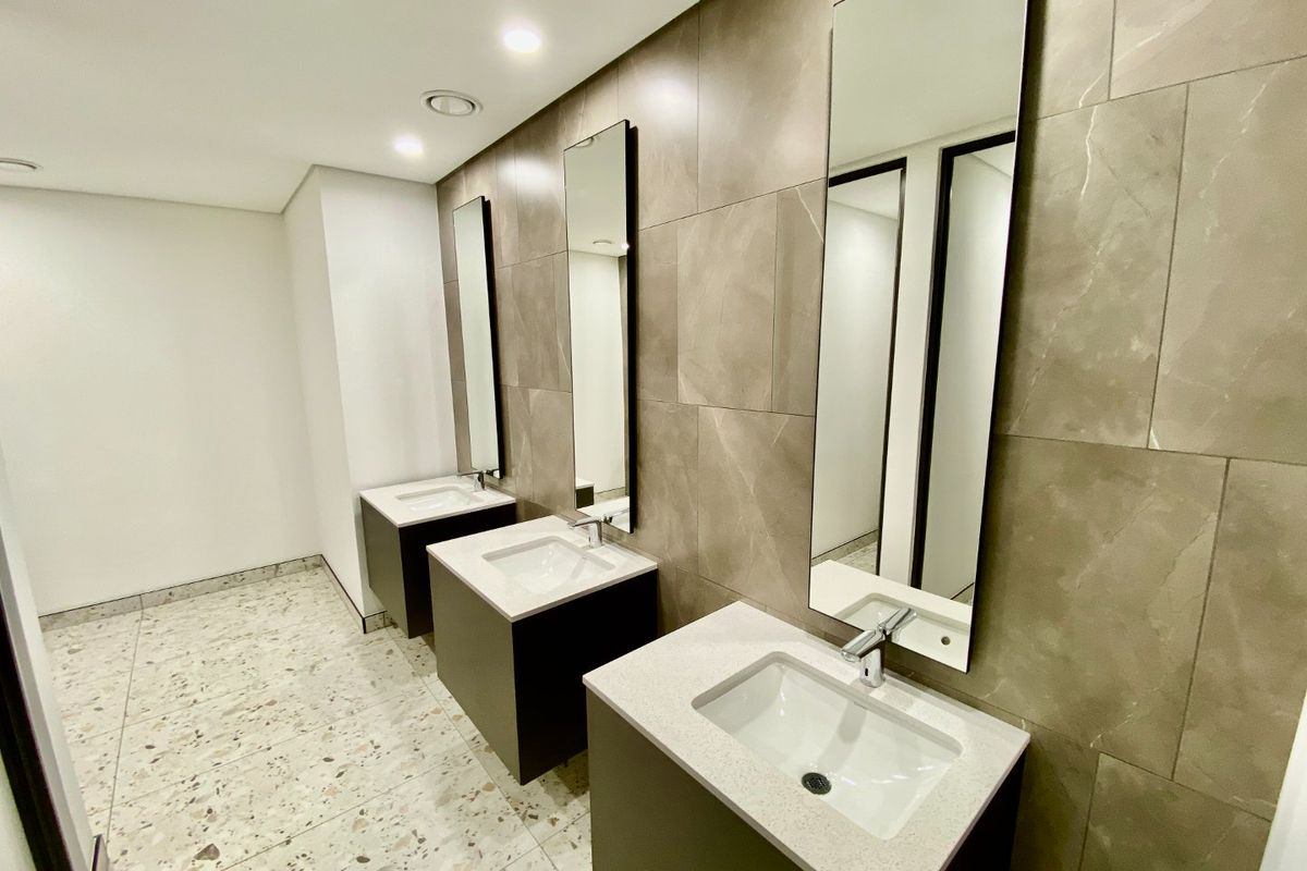 Modern commercial bathroom featuring three vanity stations with stone countertops, undermount sinks, large format wall tiling, and terrazzo flooring.