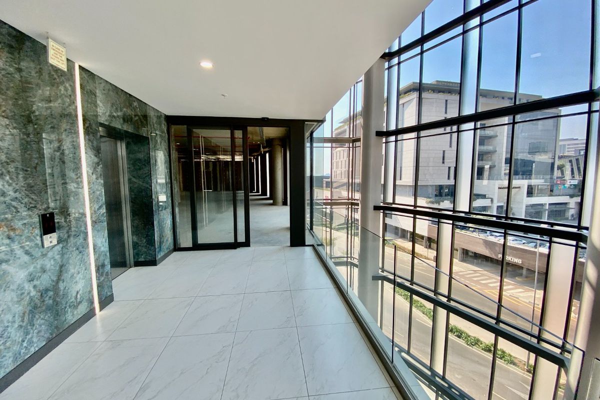 Modern commercial hallway featuring floor-to-ceiling glass windows, marble wall finishes, and high-quality porcelain tiling with elevator access.