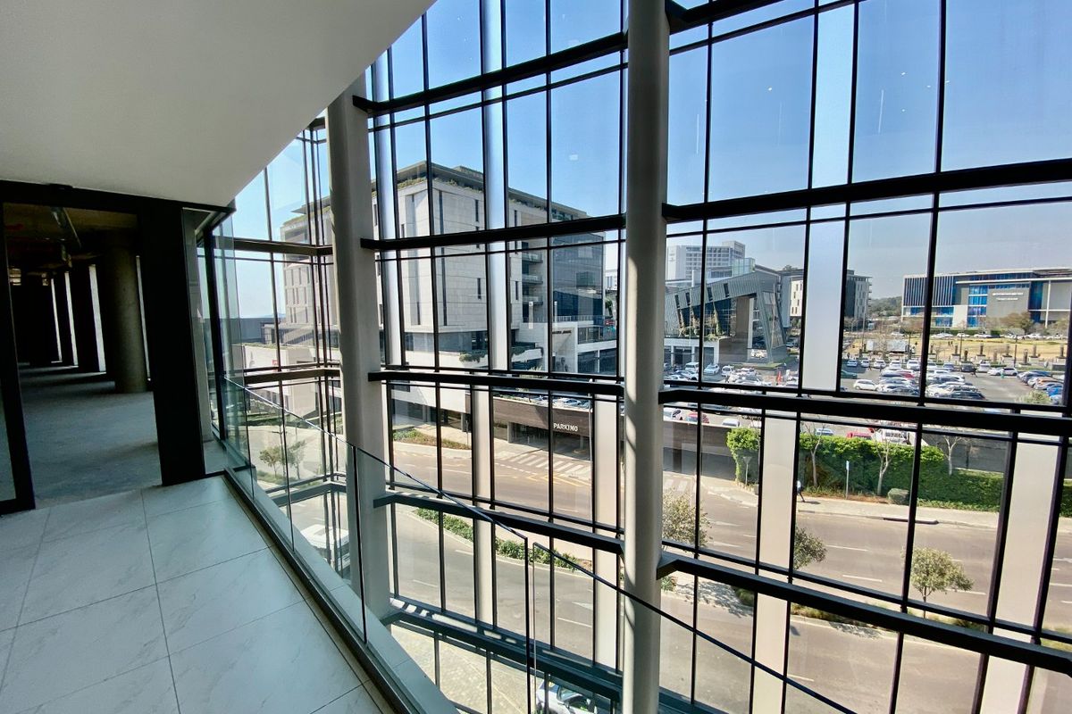 Modern commercial hallway featuring floor-to-ceiling glass curtain walls, sleek glass balustrades, and large format tiling with expansive views of the surrounding business district.