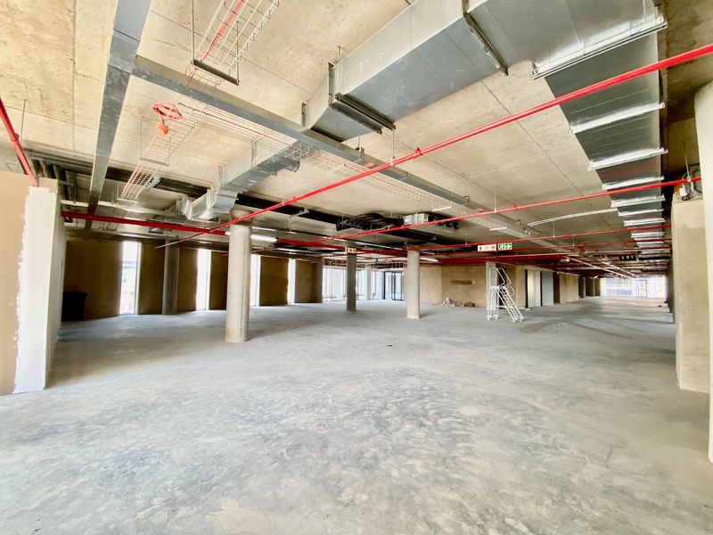 Large open-plan commercial space in shell condition featuring exposed concrete ceilings, industrial HVAC ducting, and fire suppression systems.