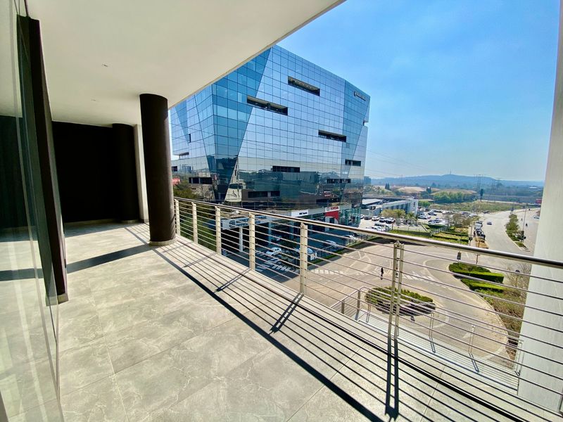 A modern, covered balcony featuring tiled flooring and a stainless steel balustrade, offering an elevated view of the surrounding commercial area.