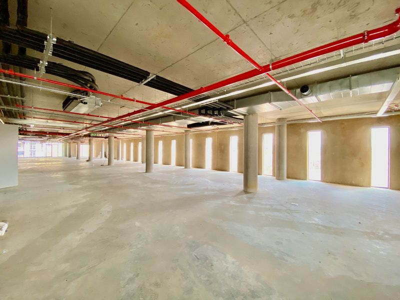 A large, open-plan commercial space featuring an industrial aesthetic with exposed concrete ceilings, ducting, and fire sprinkler systems.