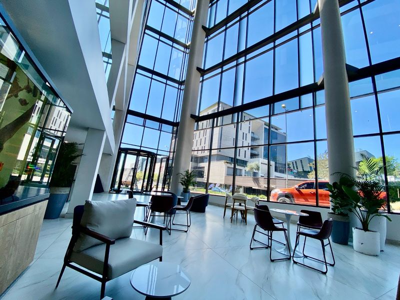 Spacious commercial lobby featuring double-volume ceilings, floor-to-ceiling glass curtain walls, and polished marble-look tile flooring.