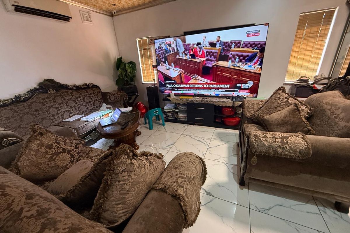 A living room featuring large format white marble-look floor tiles, wall-mounted air conditioning unit, and dual windows with fitted blinds.