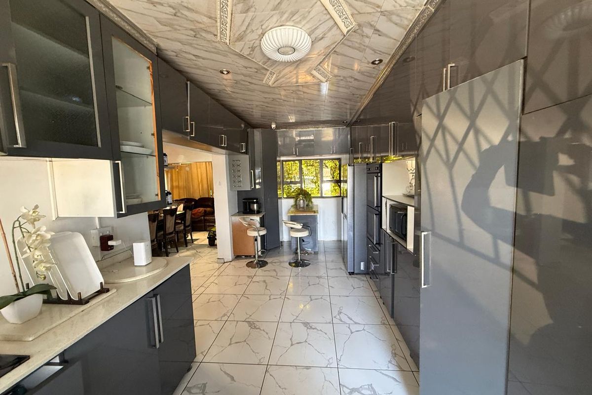 Modern kitchen featuring high-gloss grey cabinetry, marble-look floor tiles, and integrated appliances, leading into an adjacent dining area.