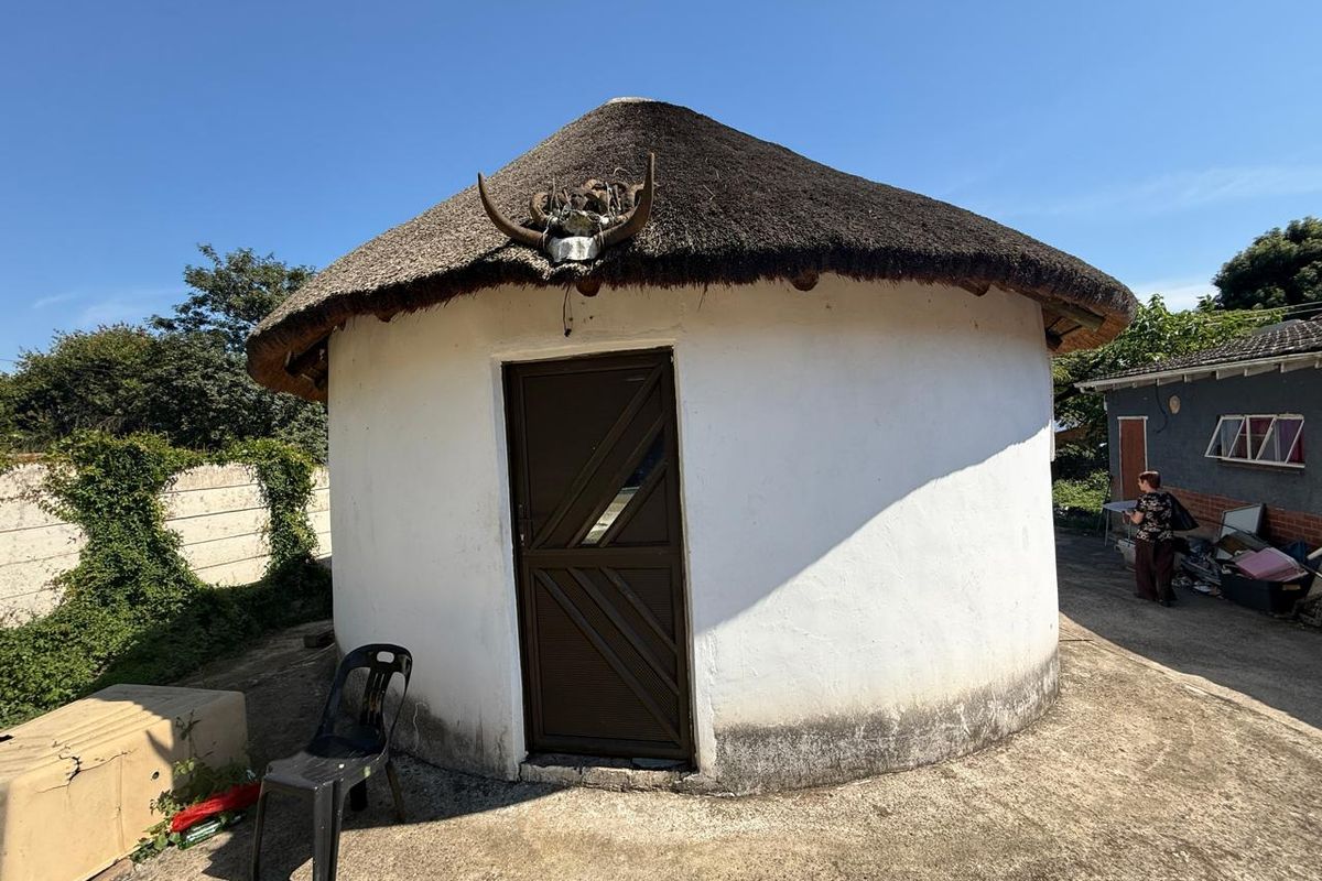 A traditional round structure with a thatched roof and white exterior walls, situated on a concrete paved area.