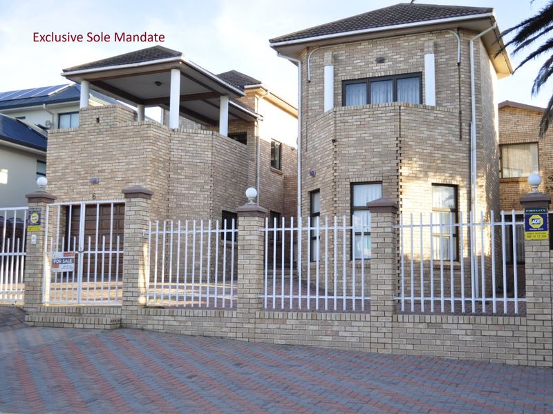 Front elevation of a double-story face brick house featuring a paved driveway, perimeter fencing, and an upper-level balcony.