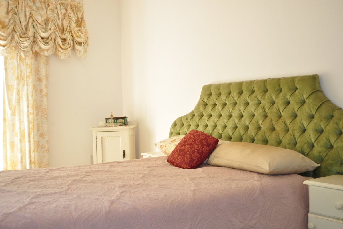 A bedroom featuring a tufted green headboard and neutral wall finishes, providing a comfortable and functional sleeping space.