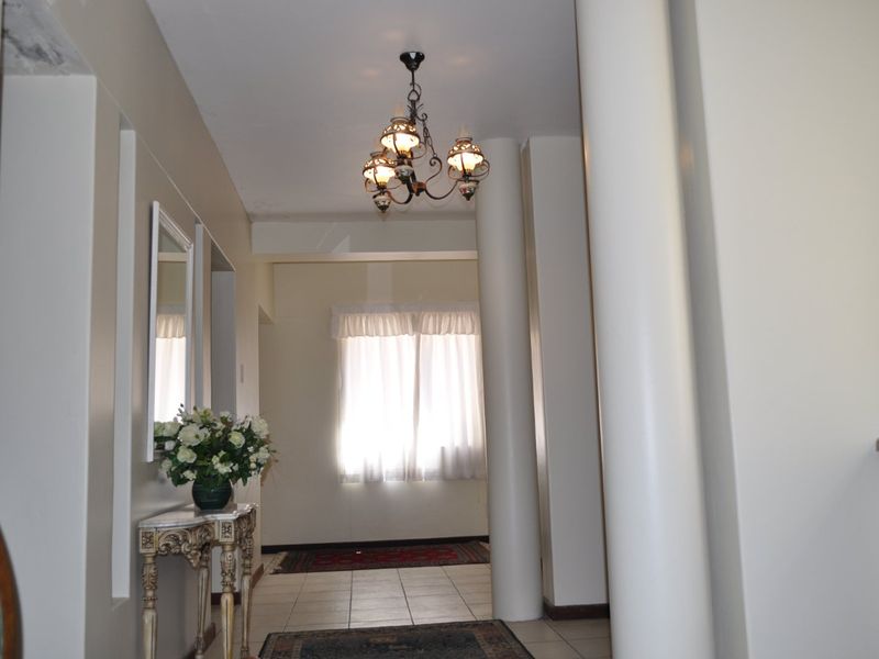 A spacious hallway featuring structural columns, tiled flooring, and a decorative chandelier, showing signs of ceiling wear and water damage.