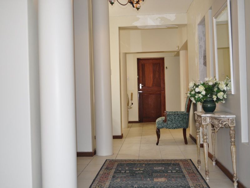 Spacious hallway featuring architectural columns, tiled flooring, and a solid timber door, requiring some cosmetic attention to the ceiling and wall finishes.