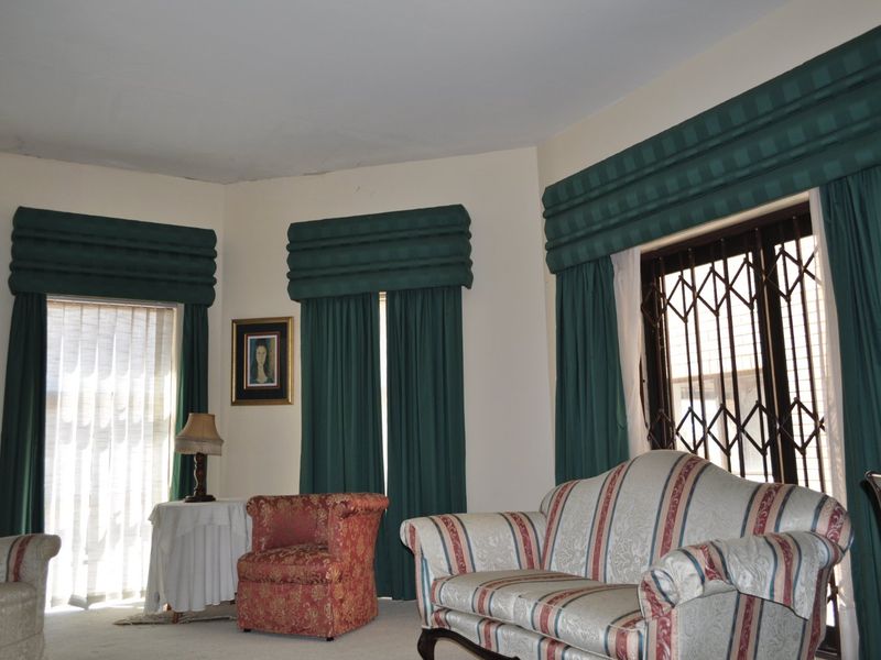 A living room featuring large windows with security gates and custom curtain pelmets, offering a traditional layout with potential for modern updates.