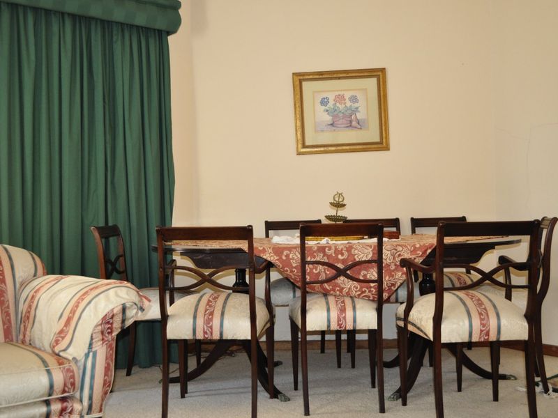 A traditional dining room area featuring carpeted flooring and floor-to-ceiling curtains, providing a functional space for family meals.