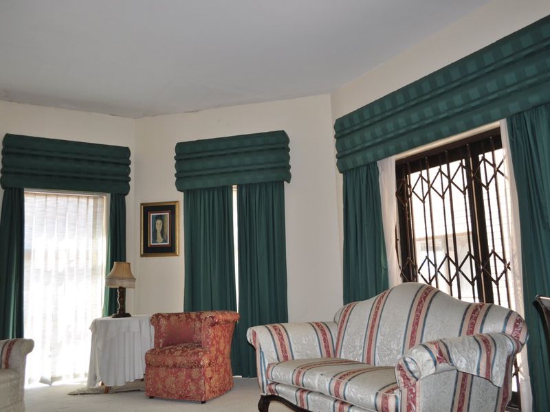 A living room featuring large windows with fitted pelmets, security gates, and sliding glass doors, offering potential for a modern update.