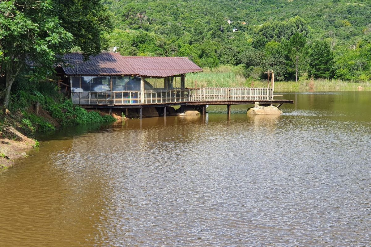 A scenic view of a lakeside structure featuring a timber deck and balustrade, set against a lush green mountain backdrop.