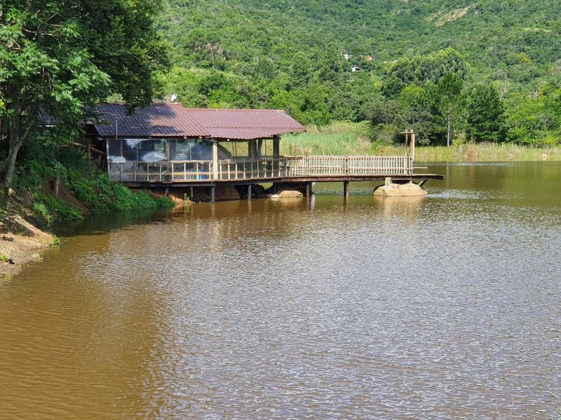 A scenic view of a lakeside structure featuring a timber deck and balustrade, set against a lush green mountain backdrop.