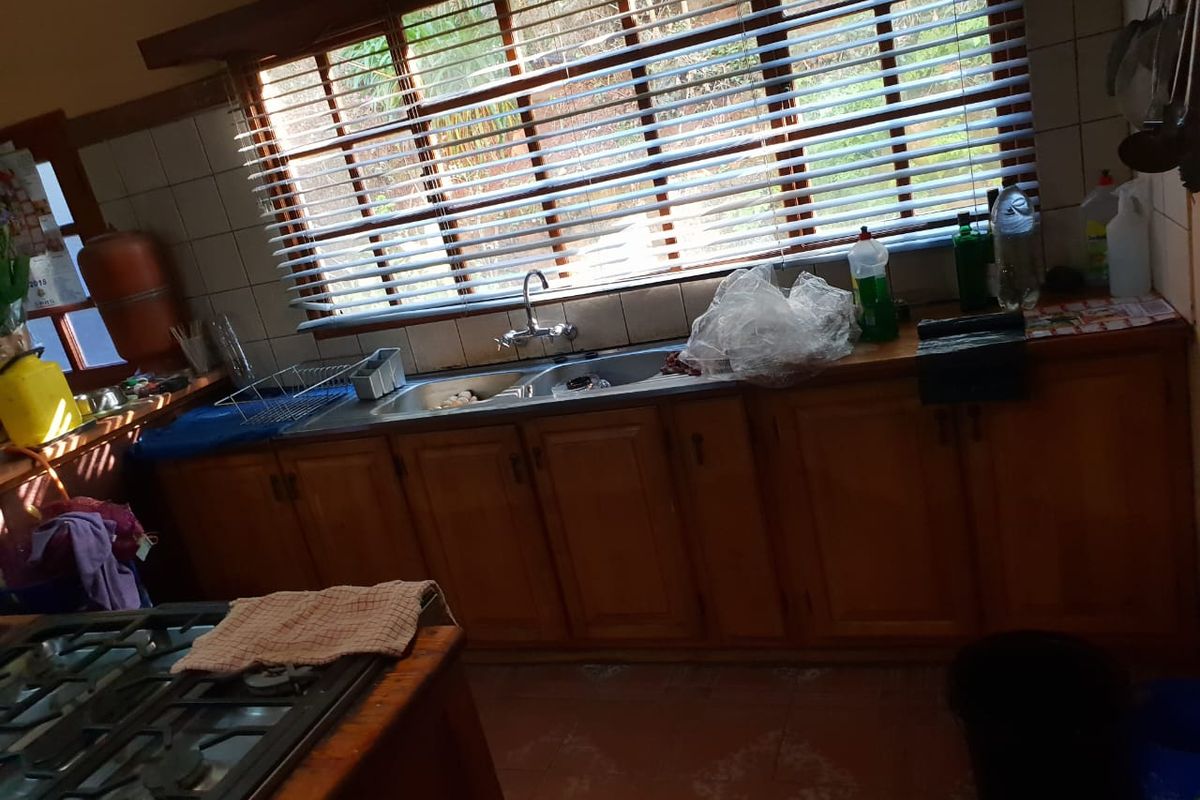 A functional kitchen featuring wooden cabinetry, a double basin sink, tiled backsplash, and a built-in gas hob with tiled flooring.