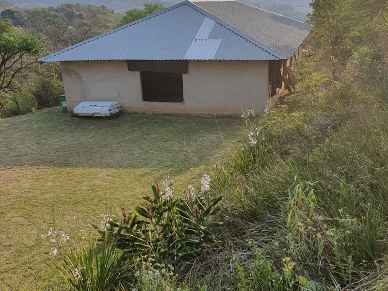 Rear view of a farm building featuring plastered walls and a corrugated metal roof set against a scenic mountain landscape.