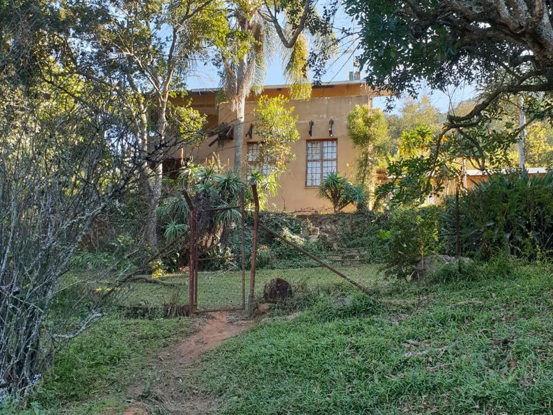 Rear view of the farm property featuring a rustic metal gate, stone retaining wall, and established garden surroundings with mature trees.