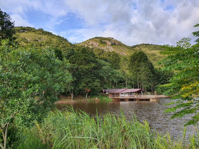 A scenic view of a tranquil lake featuring a wooden deck structure nestled against a lush, mountainous landscape.