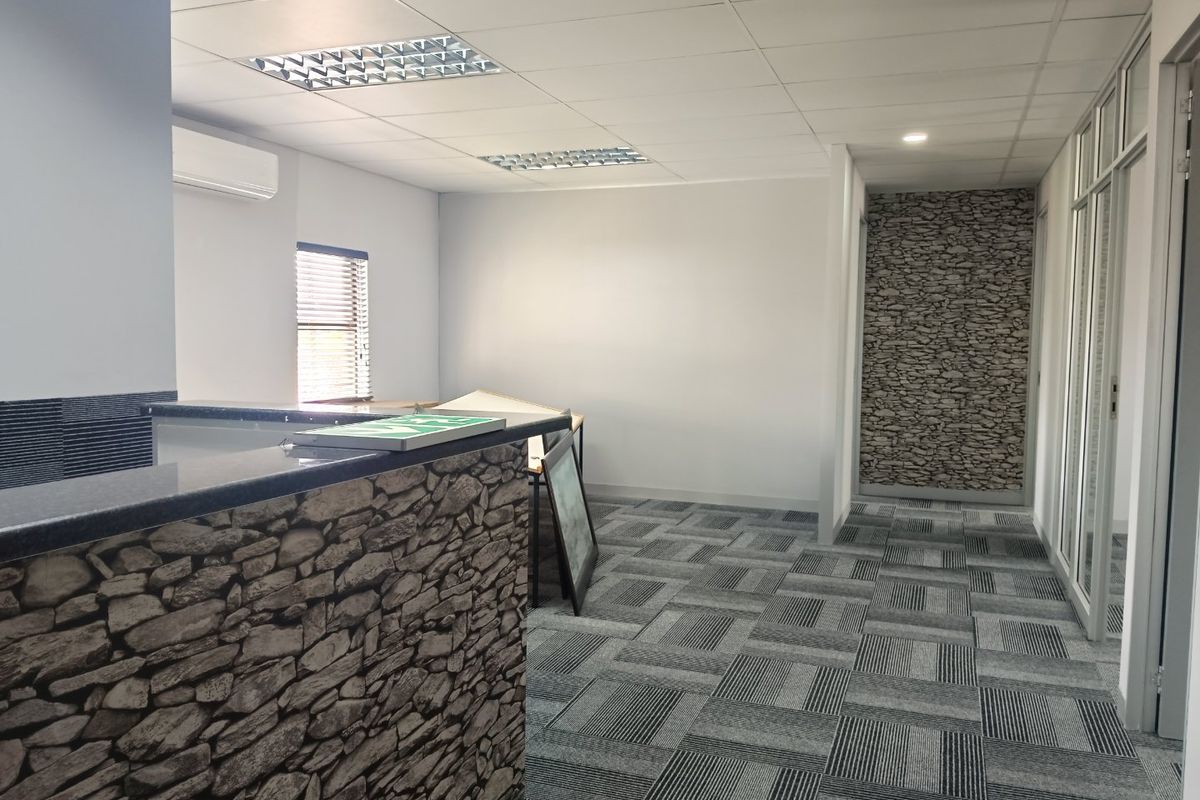 A modern commercial office space featuring a stone-clad reception desk, carpet tiles, suspended ceilings with recessed lighting, and glass partition walls.