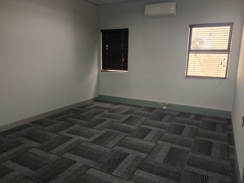 A clean, empty office space featuring grey carpet tiles, split-system air conditioning, and windows fitted with venetian blinds.