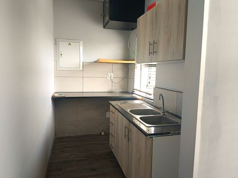 A compact, functional scullery area featuring modern wood-finish cabinetry, granite countertops, a double sink, and tiled backsplash.