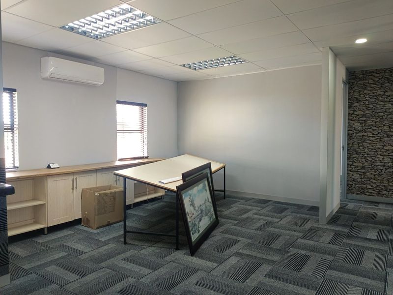 A clean, professional office space featuring carpet tiles, built-in cabinetry, a split-system air conditioner, and a decorative stone-effect feature wall.