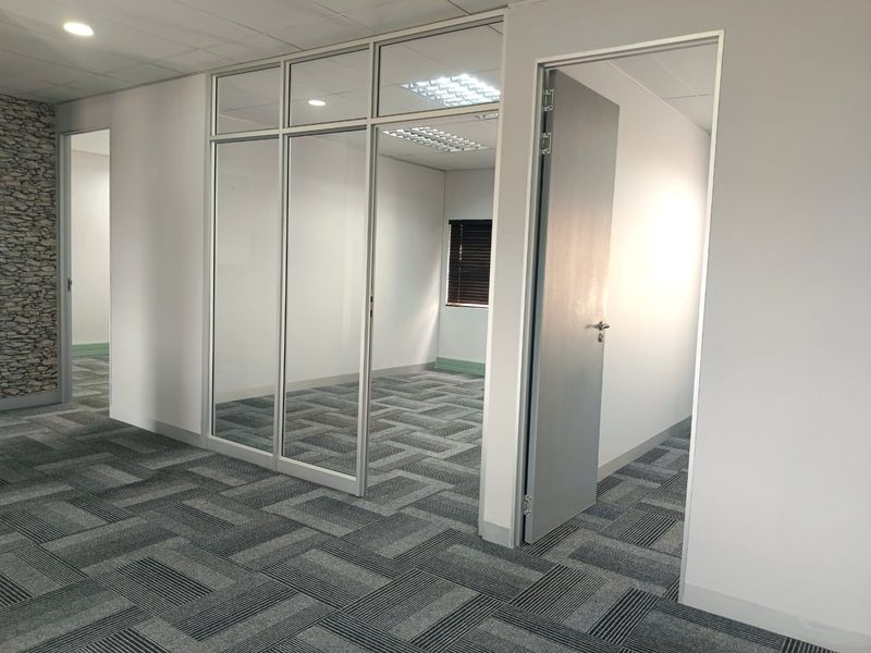 Modern commercial office space featuring glass partitions, suspended ceilings with recessed lighting, and durable carpet tile flooring.